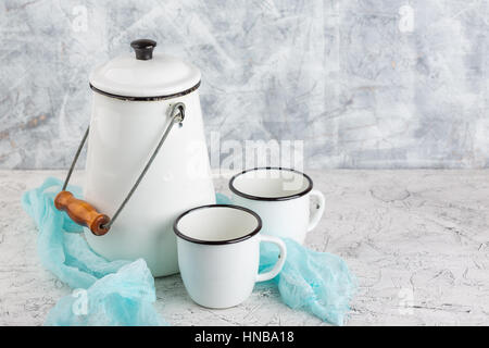 Two white cups and white enameled cans on light background Stock Photo