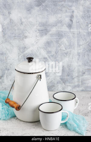 Two white cups and white enameled cans on light background Stock Photo