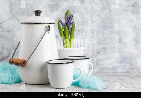 Two white enamel mugs, white can and blossoming flower hyacinth in pot on light background Stock Photo