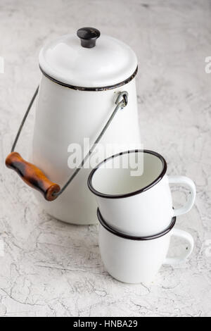 Two white cups and white enameled cans on light background Stock Photo