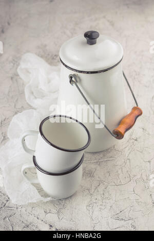 Two white cups and white enameled cans on light background Stock Photo