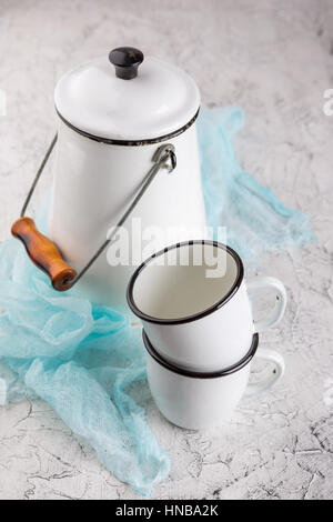 Two white cups and white enameled cans on light background Stock Photo