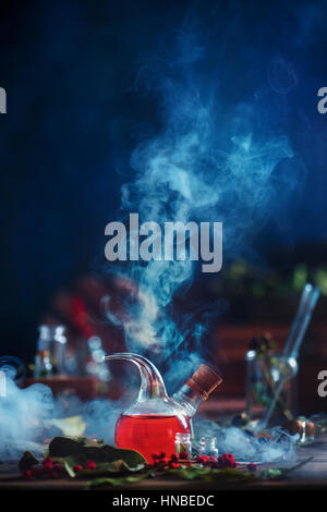 Laboratory retort with red liquid and thick clouds of rising smoke on a dark blue background Stock Photo