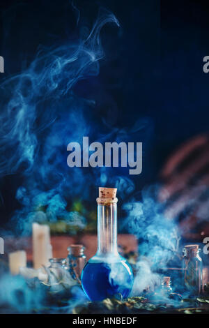Glass bottle with blue liquid and thick clouds of rising smoke on a dark blue background Stock Photo