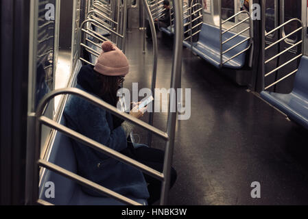 Young woman in warm clothes using mobile phone while sitting in subway train Stock Photo