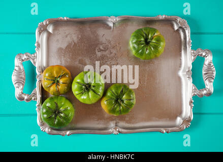green heirloom tomatoes on silver tray on Iris Blue background Stock Photo