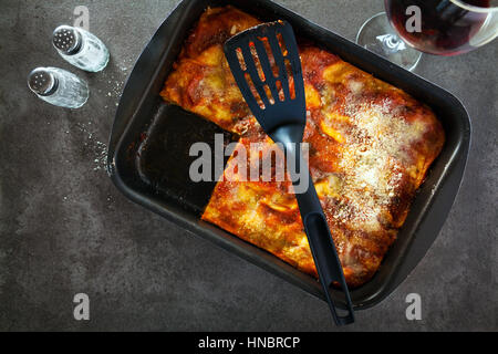 classic Italian eggplant Lasagna with vegetables and red wine in baking dish on a gray stone background .spilled parmesan, rosemary, old spoon . View  Stock Photo