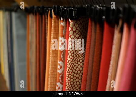 A rack of  patterned upholstery fabric samples hung closely together on black plastic hangers, solid colors and patterns, reds, pink, ochre, blue hues Stock Photo