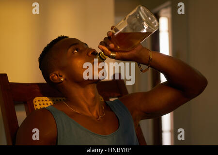 Social issues, substance abuse with alcoholic young black man drinking alchool from liquor bottle at home. Stock Photo