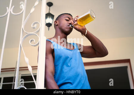 Social issues and substance abuse. Alcoholic young black man drinking alchool from liquor bottle at home, looking at camera Stock Photo