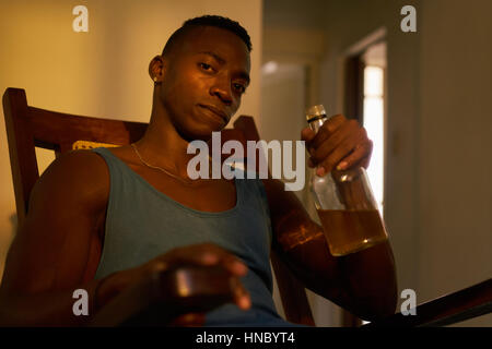 Social issues, substance abuse with alcoholic young black man drinking alchool from liquor bottle at home, looking at camera holding bottle of whiskey Stock Photo