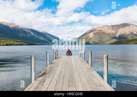 Woman sitting on dock, view of Lake Rotoiti, Nelson Lakes National Park, Tasman District, Southland, New Zealand Stock Photo