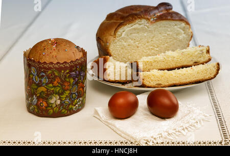 On the table on a white napkin are two painted Easter eggs, next on the plate of sliced cake. Stock Photo