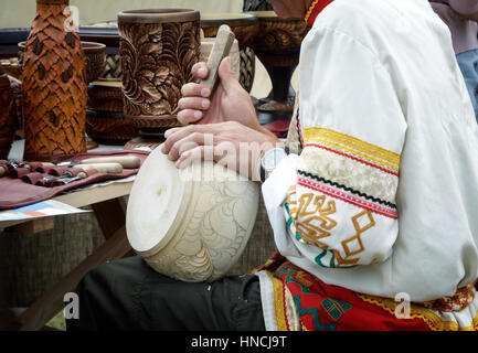 The revival of the ancient craft: man in national costume is decorated with carved wooden dishes with the help of special tools. Stock Photo