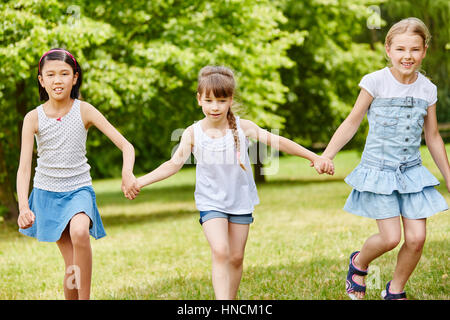 Three girls as friends walk together in the park holding hands Stock Photo