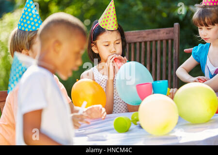 Children celebrate with colorful balloons and hats at birthday party in garden Stock Photo