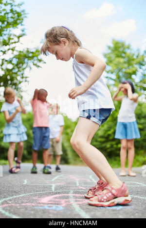 Girl jumps with concentration at hopscotch game in summer Stock Photo