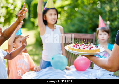 Kids excited about cake at childrens birthday party in summer Stock Photo