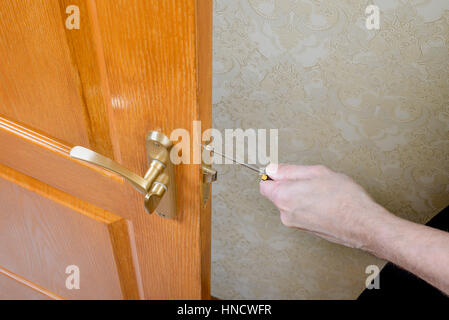 A man is mounting the protection strike of the deadbolt on a door with a classical curved style bronze handle using a screwdriver Stock Photo