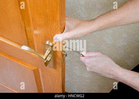 A man is mounting the protection strike of the deadbolt on a door with a classical curved style bronze handle using a screwdriver Stock Photo