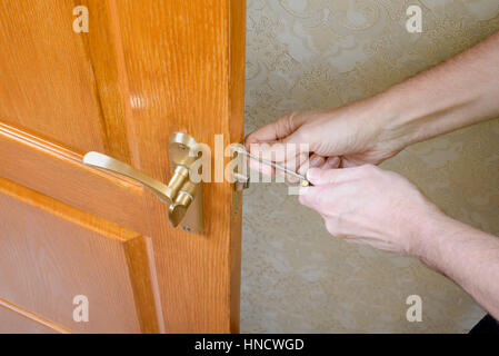 A man is mounting the protection strike of the deadbolt on a door with a classical curved style bronze handle using a screwdriver Stock Photo