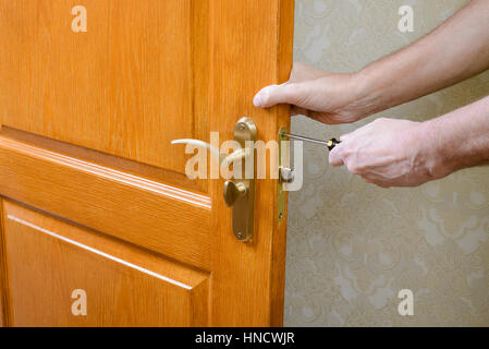 A man is mounting the protection strike of the deadbolt on a door with a classical curved style bronze handle using a screwdriver Stock Photo