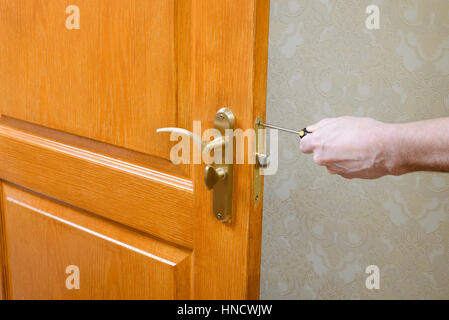 A man is mounting the protection strike of the deadbolt on a door with a classical curved style bronze handle using a screwdriver Stock Photo