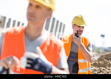 Middle-aged male worker using walkie-talkie with colleague in foreground at construction site Stock Photo