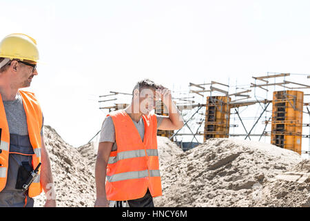 Construction worker looking at tired colleague wiping sweat at site Stock Photo