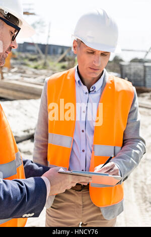 Engineers writing on clipboard at construction site Stock Photo