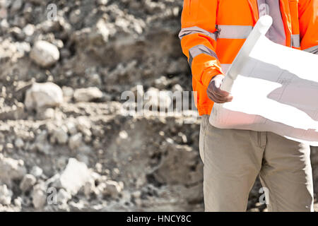Midsection of supervisor holding blueprint at construction site Stock Photo