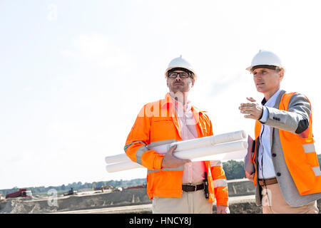 Supervisors with blueprints discussing at construction site against clear sky Stock Photo