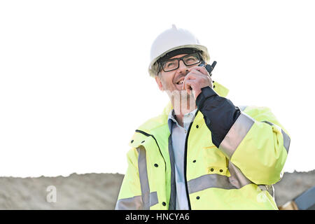 Happy supervisor using walkie-talkie at construction site against clear sky Stock Photo