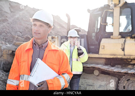 Engineer holding clipboard on construction site with colleague in background Stock Photo