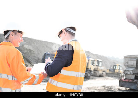 Happy engineers discussing over clipboard at construction site against clear sky Stock Photo