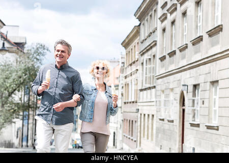 Happy middle-aged couple holding ice cream cones while walking in city Stock Photo