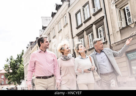 Middle-aged man showing something to friends while walking in city Stock Photo