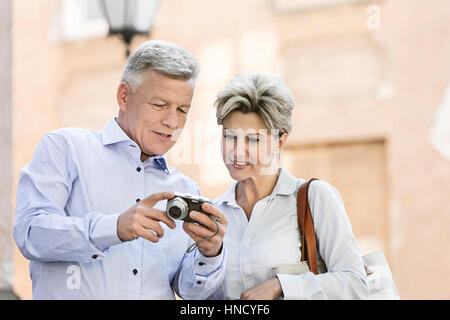 Smiling middle-aged couple reviewing photos on digital camera outdoors Stock Photo