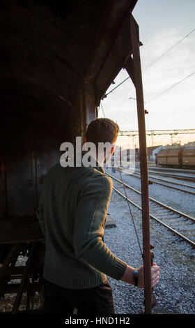 Fit guy in green sweater traveling in old rusty train looking at sunset Stock Photo