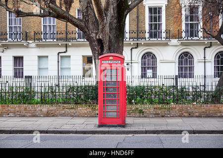 Iconic red London phone booth in front of a block of residential building and a big tree in the Paddington area Stock Photo