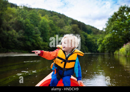 Happy kid enjoying kayak ride on beautiful river. Little curly toddler boy kayaking on hot summer day. Water sport and camping fun. Canoe for children Stock Photo