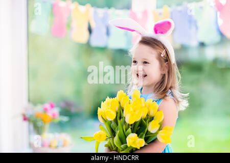 Happy little girl in bunny ears holding tulip flower bouquet. Kids celebrate Easter. Children having fun on Easter egg hunt. Home decoration, pastel b Stock Photo