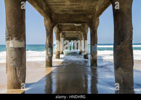 Standing beneath Manhattan Beach Piere as waves crash from the Pacific Ocean Stock Photo