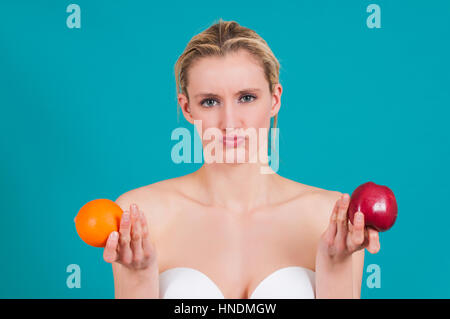 Confused young woman holding an apple and an orange Stock Photo