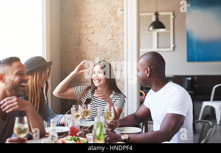 Group of four attractive friends dining at table and having fun while conversation in light modern cafe. Stock Photo