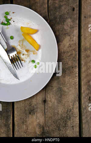 Overhead view of leftovers on a plate with knife and fork on a rustic wooden background Stock Photo