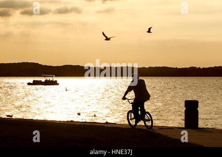 a bicyclist rides along the beach at sunset Stock Photo
