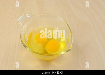 Two raw eggs in glass measuring cup on wooden table Stock Photo