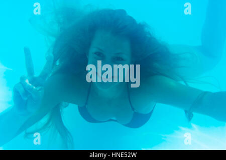 Model release, Junge Frau schwimmt unter Wasser und macht Fingerzeichen - woman under water Stock Photo