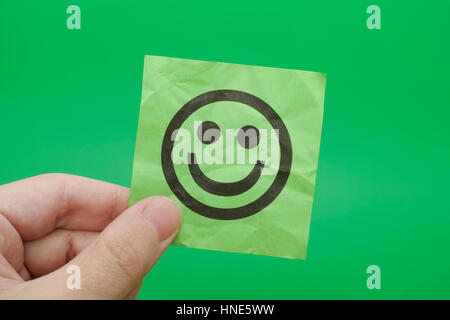 Person holding green paper note with Happy Face in his hand. Green background. Stock Photo